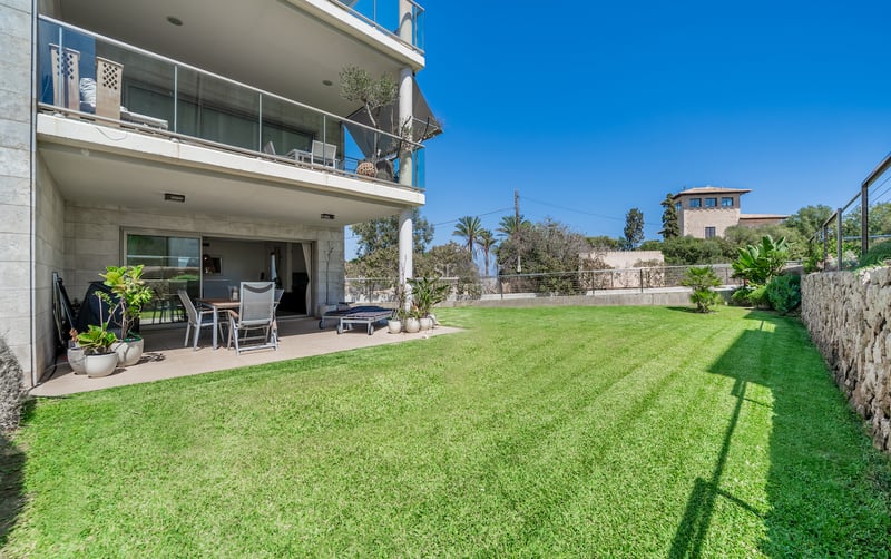 Terrasse couverte avec mobilier d'extérieur ouvrant sur un grand jardin privé gazonné sous un ciel bleu.