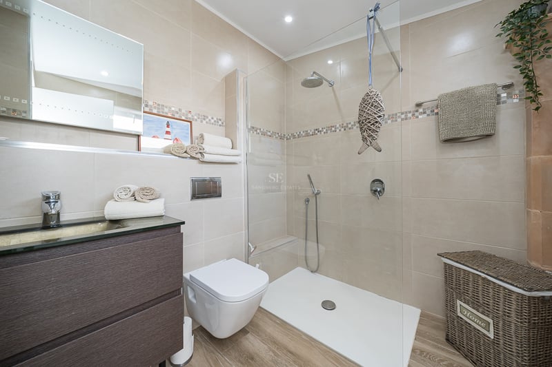 Salle de bains contemporaine avec douche vitrée, meuble vasque en bois sombre et carrelage beige.