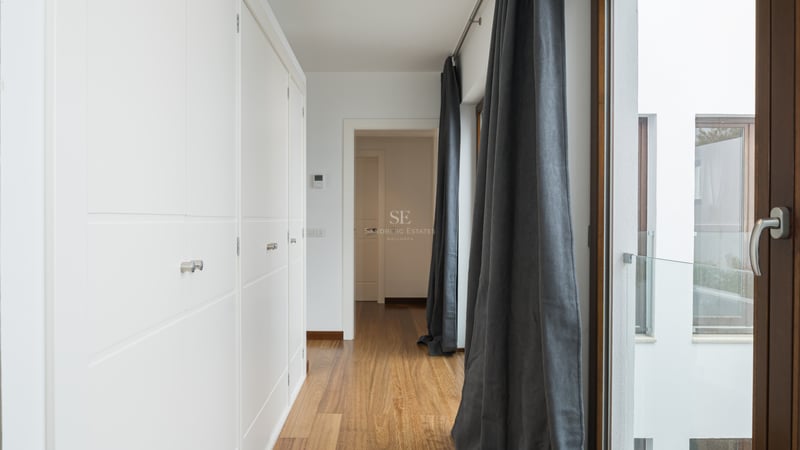 Couloir lumineux avec de grands placards blancs intégrés, parquet en bois chaleureux et rideaux gris anthracite.