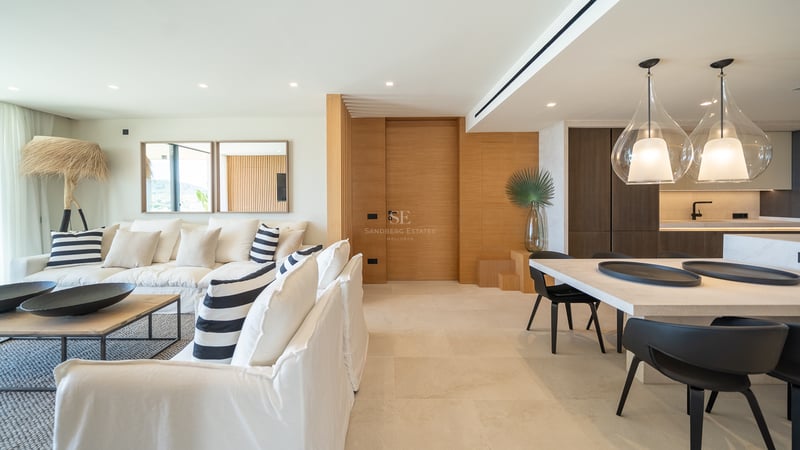 Salon moderne à aire ouverte avec canapés blancs, accents en chêne et salle à manger avec suspensions en verre design.