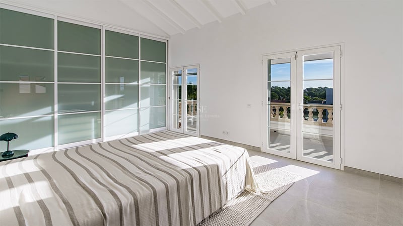 Ljust sovrum med randig säng, högt ryggåstak, garderober i frostat glas och dörrar till en balkong.