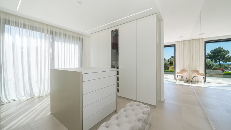 Dressing spacieux avec placards blancs, îlot central, pouf capitonné et vue sur mer par les grandes baies vitrées.