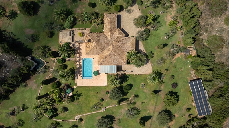 Vue aérienne d'une grande villa méditerranéenne avec piscine, jardins paysagers et panneaux solaires.
