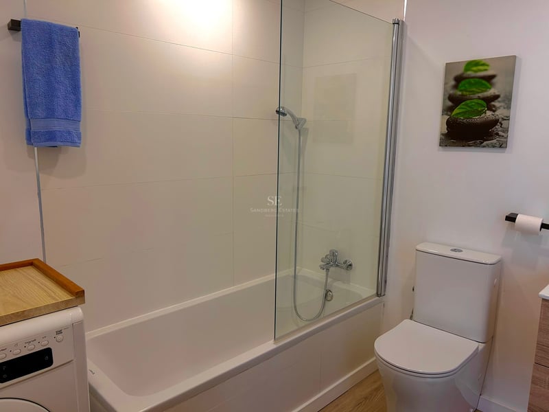 White bathroom featuring a bathtub with glass partition, toilet, and washing machine.