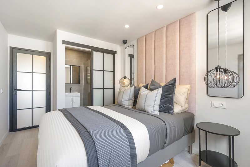 Zeitgenössisches Schlafzimmer mit rosa Samtkopfteil, industriellen Glastüren und Blick auf das En-Suite-Bad.