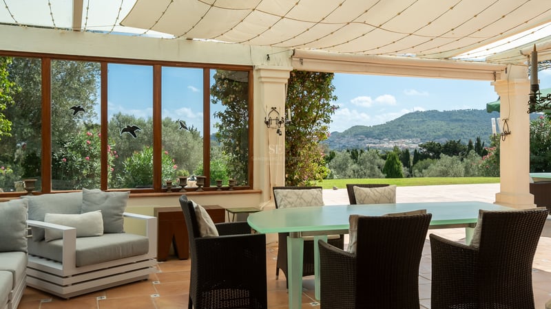 Terrasse extérieure couverte avec grande table à manger, chaises en osier et vue sur les collines et montagnes.