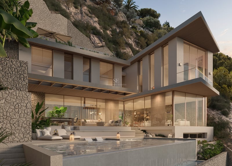 Two-story modern villa with stone walls, floor-to-ceiling glass windows, and an infinity pool at dusk.