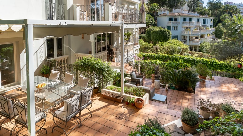 Sun-drenched Mediterranean terrace with terracotta tiles, wrought iron dining set under a white awning, and lush greenery.