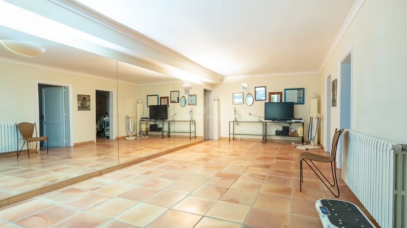 Grande pièce avec sol en terre cuite, un mur de miroirs et du matériel de fitness dans une villa de luxe.