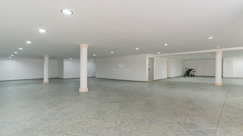 Geräumige Tiefgarage mit grauen Fliesen, weißen Wänden, LED-Einbaustrahlern und weißen Stützpfeilern.