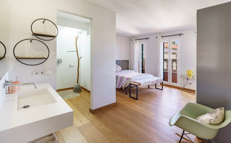 Rymligt sovrum med ljust ekparkettgolv och öppet badrum med modern vit kommod.