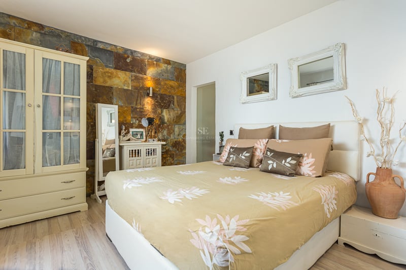 Modern view of a villa featuring an infinity pool, large windows, and minimalist design. Lush vegetation and blue sky backdrop.