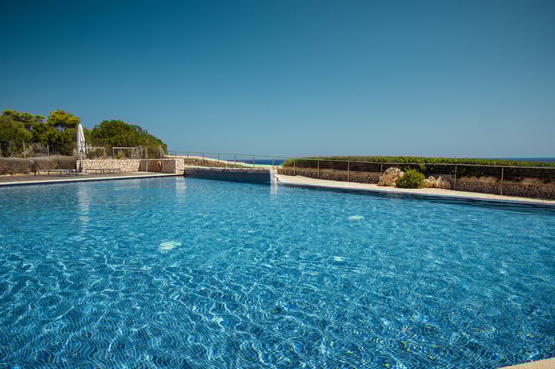 Une grande piscine carrelée en bleu entourée de murs en pierre naturelle et d'une balustrade en métal.