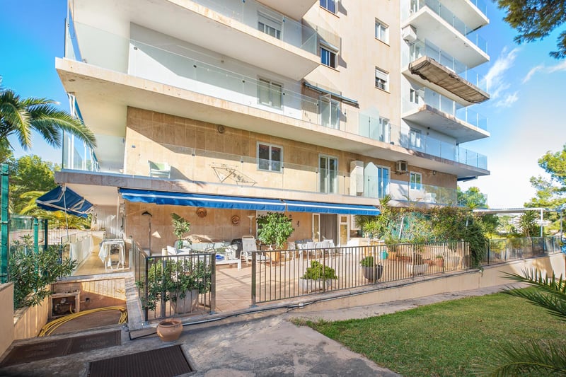 Mehrstöckiges Wohngebäude mit Natursteinverkleidung, Glasbalkonen und großer Terrasse mit blauer Markise.