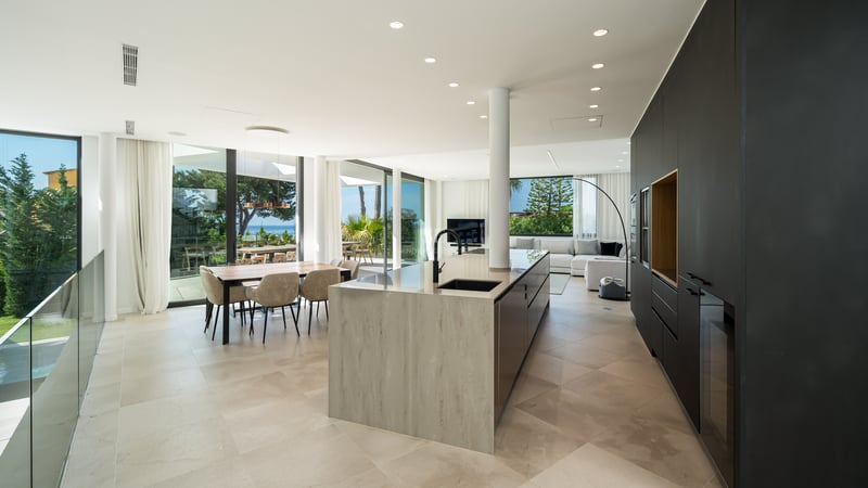 Cuisine ouverte avec grand îlot en pierre, armoires sombres et coin repas avec baies vitrées toute hauteur.