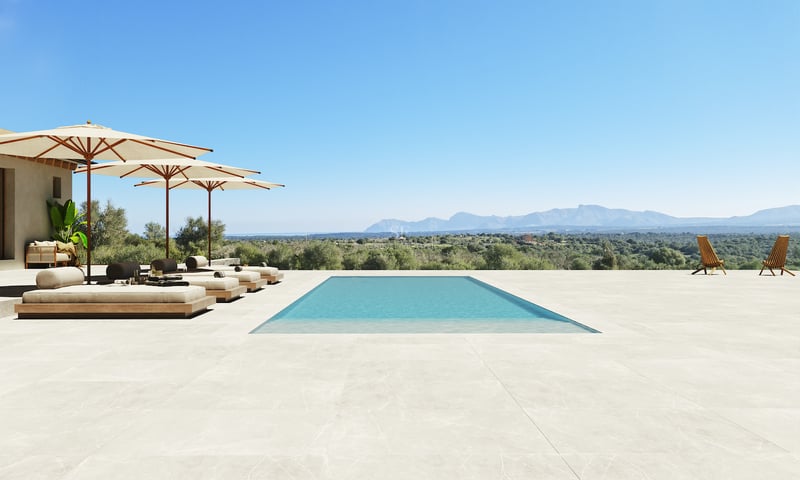 Piscine rectangulaire sur une vaste terrasse en pierre dominant un paysage montagneux sous un ciel bleu pur.