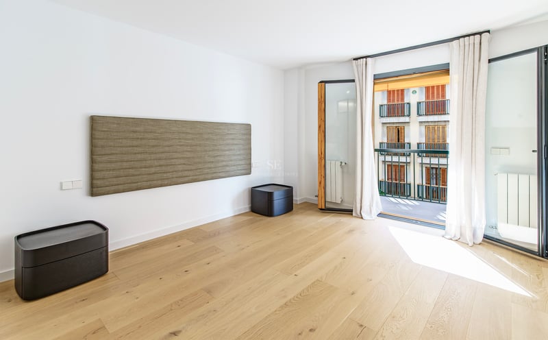 Chambre moderne avec parquet en bois clair, tête de lit murale texturée et balcon baigné de lumière naturelle.