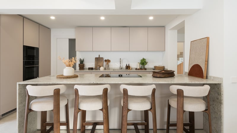Modern kitchen with beige cabinets, a large stone island, and four wood and fabric bar stools.