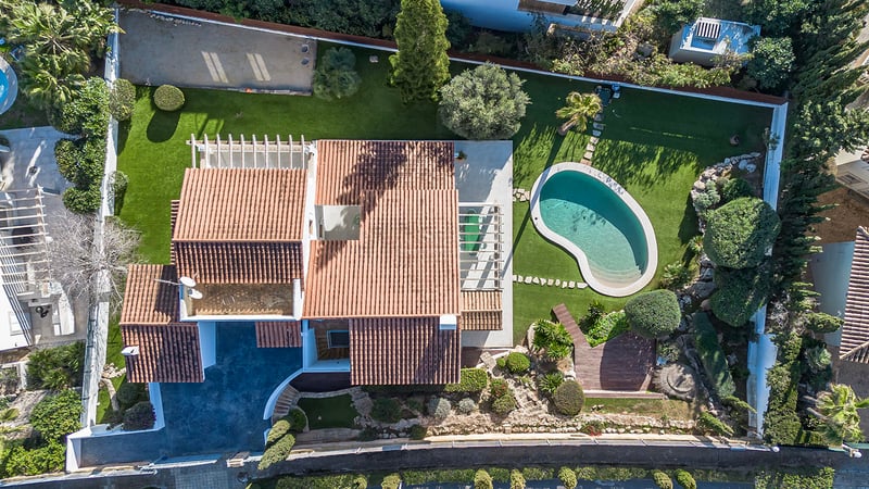 Fågelperspektiv av en lyxvilla med tegeltak, njurformad pool och välskötta trädgårdar.