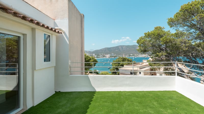 Terrasse avec gazon artificiel et garde-corps blanc surplombant une baie bleue avec des yachts et des montagnes.