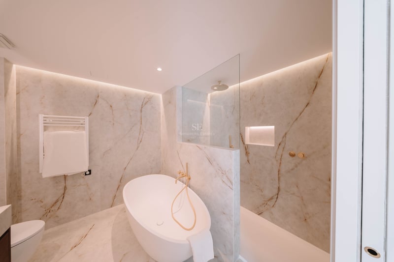 Salle de bain élégante avec baignoire îlot, douche à l'italienne et murs en marbre avec robinetterie dorée.