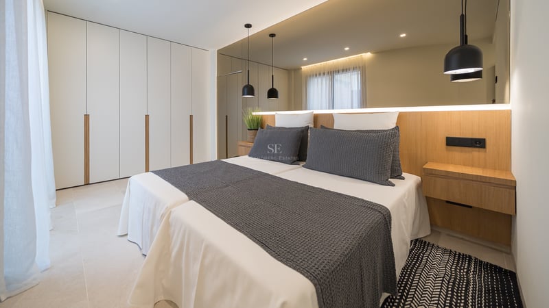 Chambre moderne avec lits jumeaux, placards blancs du sol au plafond, tête de lit en chêne et grand miroir mural.