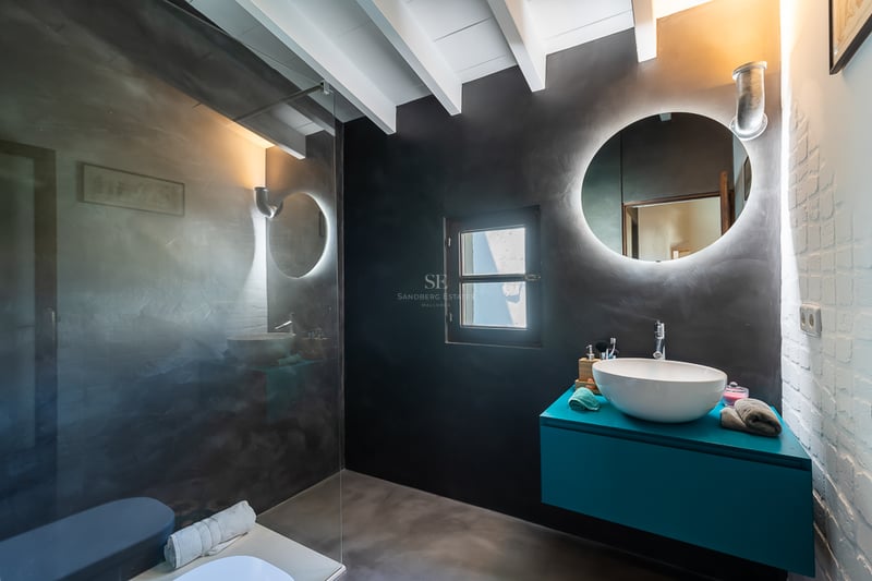 Salle de bains contemporaine avec murs en béton ciré anthracite, meuble vasque turquoise et miroir rond rétroéclairé.