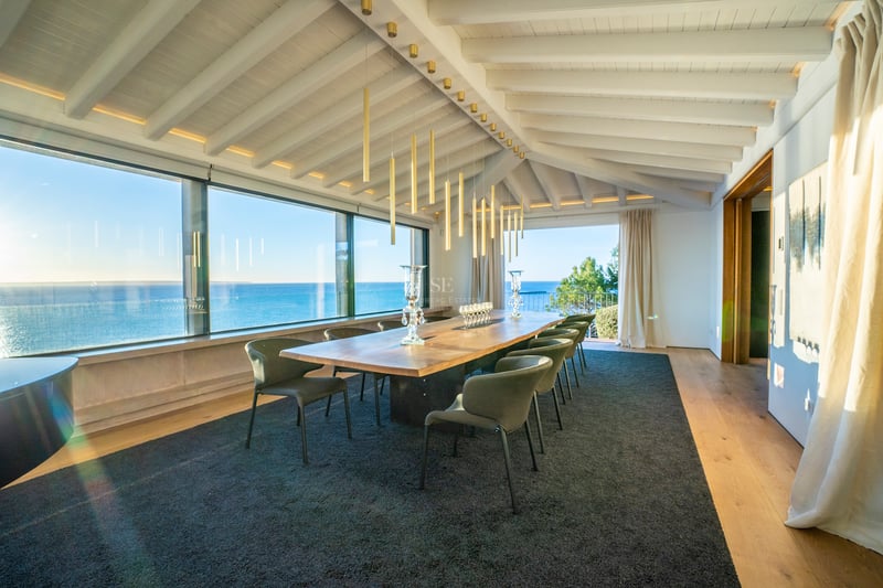 Luxuriöses Esszimmer mit Massivholztisch, Designerstühlen und großen Fensterfronten mit Blick auf das Mittelmeer.