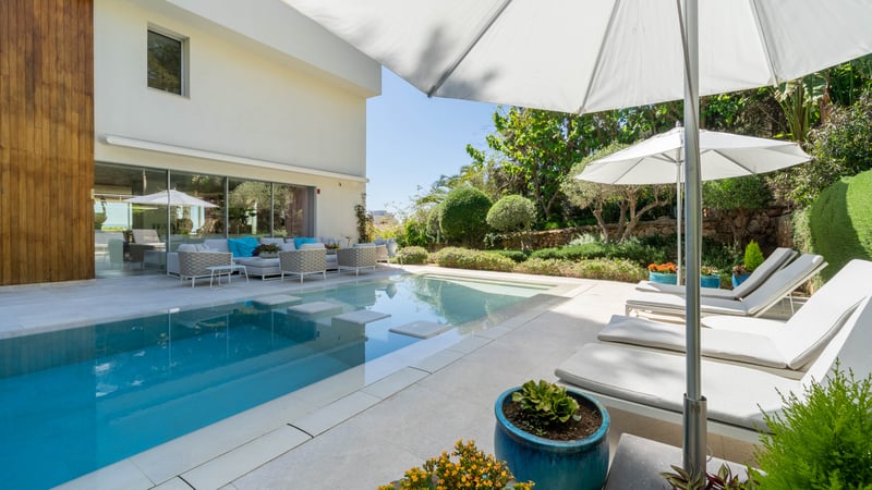 Eleganter Außenpool mit Trittsteinen, weiße Natursteinterrasse, Sonnenliegen und üppige Gartenbepflanzung.