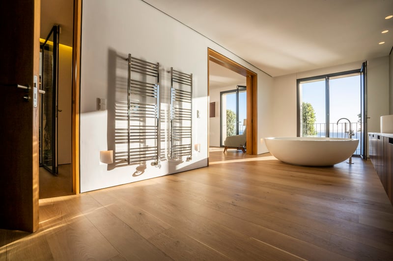 Minimalistisches Master-Bad mit Eichenparkett, ovaler freistehender Badewanne, verchromten Handtuchwärmern und Meerblick.