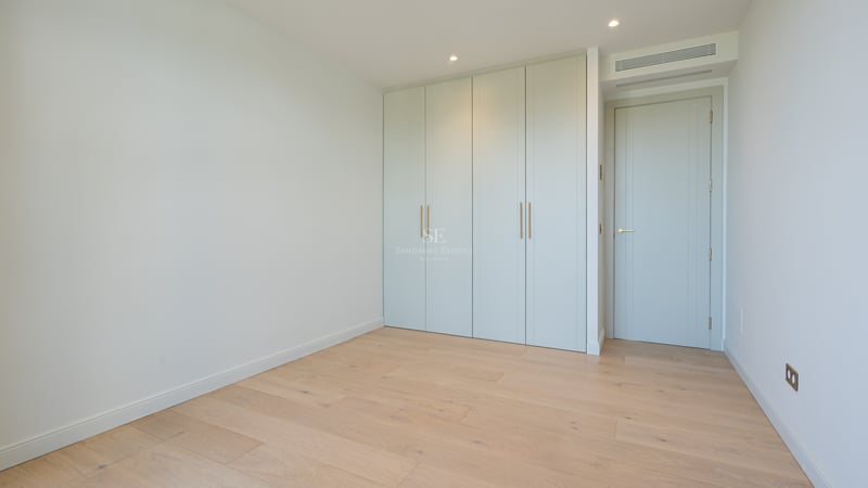 Empty room featuring light oak flooring, sage green built-in wardrobes, and minimalist white walls.