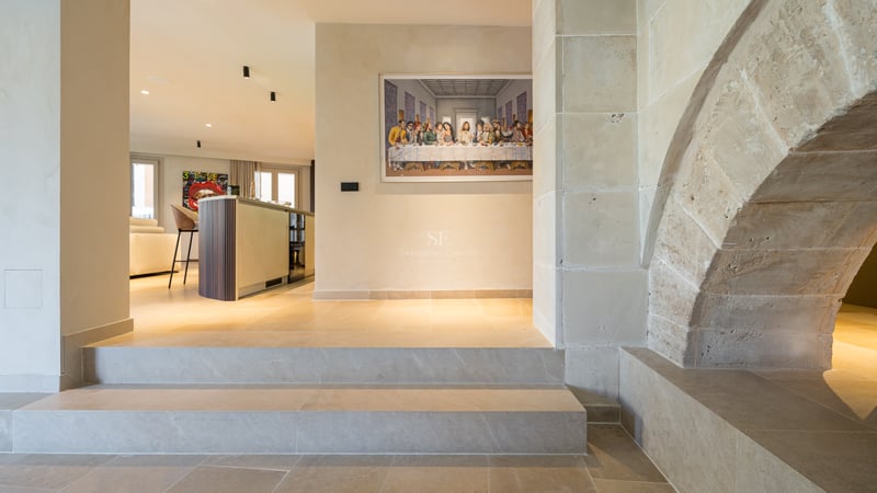 Intérieur de luxe avec une grande arche en pierre, des marches et un îlot de cuisine moderne en arrière-plan.