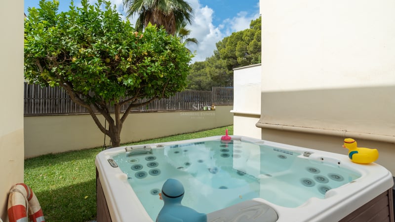 Un jacuzzi extérieur moderne dans un jardin privé à côté d'un citronnier et d'un mur blanc.