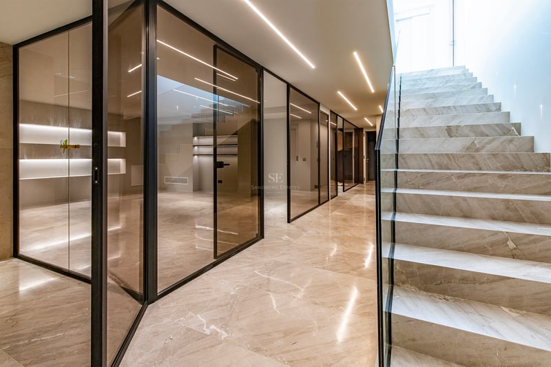 Couloir moderne avec escalier en marbre, cloisons en verre fumé et éclairage LED linéaire au plafond.