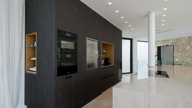 Cuisine moderne avec placards anthracite, îlot en marbre et fours Miele intégrés dans un espace lumineux.