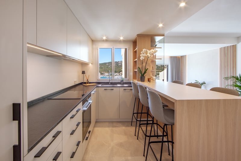 Cuisine moderne avec placards blancs, plans de travail sombres, bar en bois avec tabourets et fenêtre avec vue sur le port.