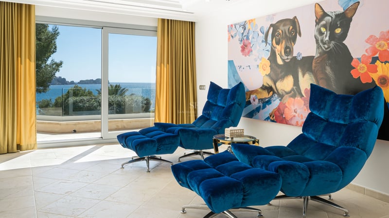 Zwei blaue Samt-Loungesessel mit Hockern in einem hellen Raum mit Blick auf das Meer durch Glasschiebetüren.