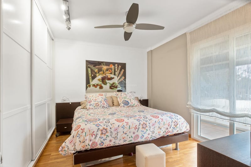 Schlafzimmer mit Eichenparkett, weißen Einbauschränken, Doppelbett und Glastür zur Terrasse.