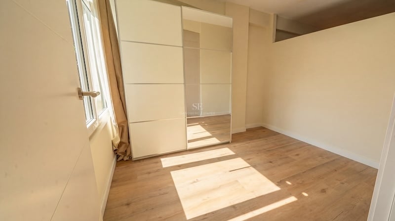 Dormitorio moderno vacío con suelo de roble claro, paredes crema y un gran armario empotrado con espejo.