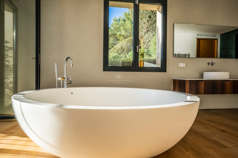 Modernes Master-Badezimmer mit großer weißer freistehender Badewanne auf Eichenparkett und Blick in den Garten.