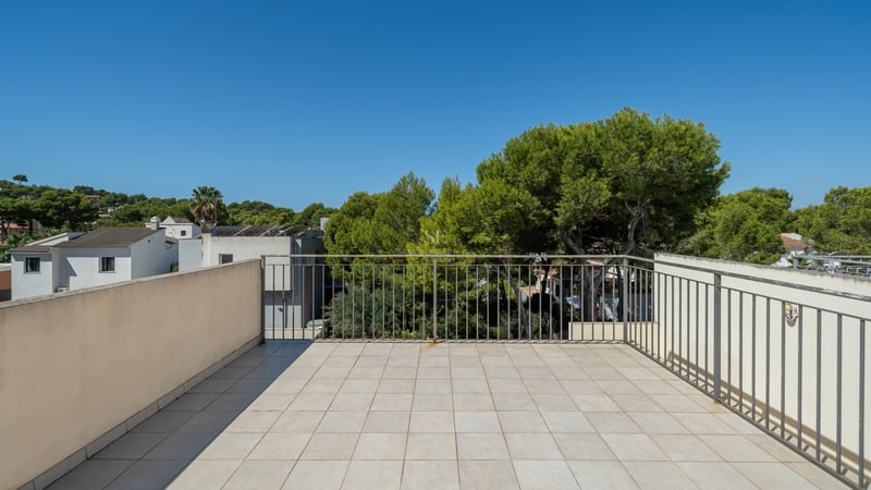Kaklad terrass med metallräcke som vetter mot gröna pinjeträd under en klarblå himmel.