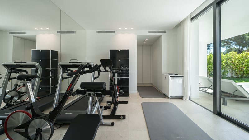 Salle de sport moderne avec vélos Keiser, tapis de course et miroirs, ouvrant sur une terrasse de jardin.