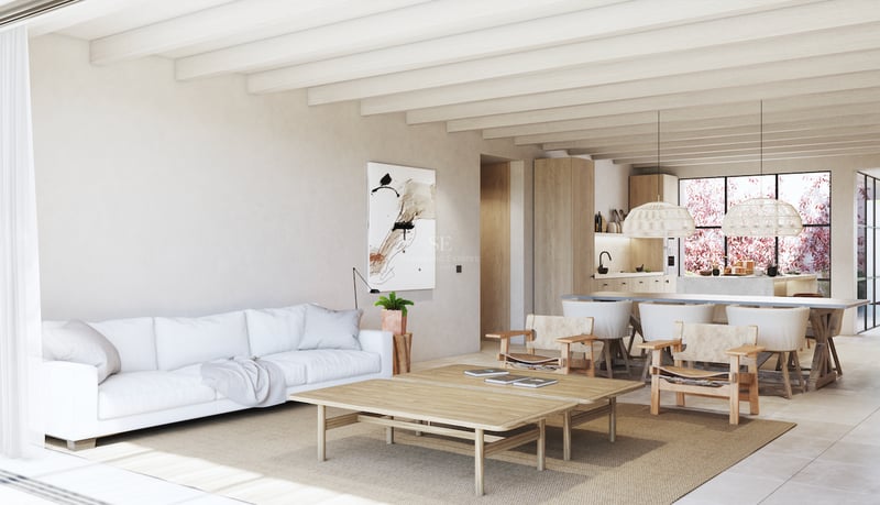 Salon lumineux avec poutres apparentes, canapé blanc, mobilier en bois clair et cuisine ouverte à l'arrière-plan.