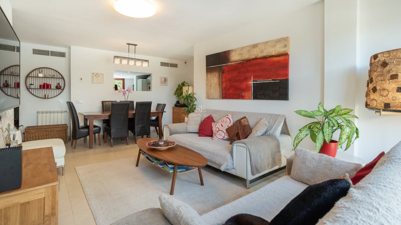 Salon lumineux avec canapés blancs, table basse en bois et coin repas avec chaises en cuir noir.