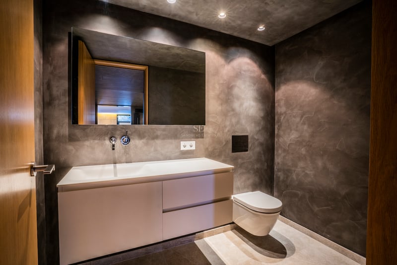 Modernes Badezimmer mit anthrazitfarbenen Mikrozementwänden, weißem Hängewaschtisch und großem Spiegel.