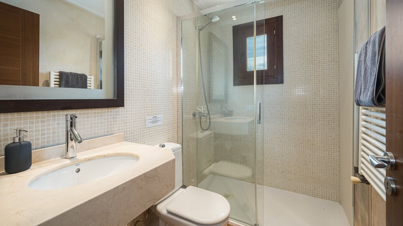 Salle de bain avec douche vitrée, murs en mosaïque beige et plan de toilette en marbre.