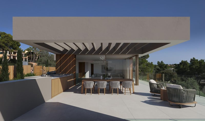 Terrasse ensoleillée avec cuisine extérieure, table en bois et fauteuils lounge face à une pinède.