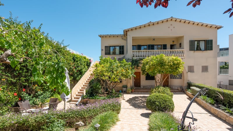 Exteriör av en medelhavsvilla i två våningar med gröna fönsterluckor, stentappa och en anlagd innergård.